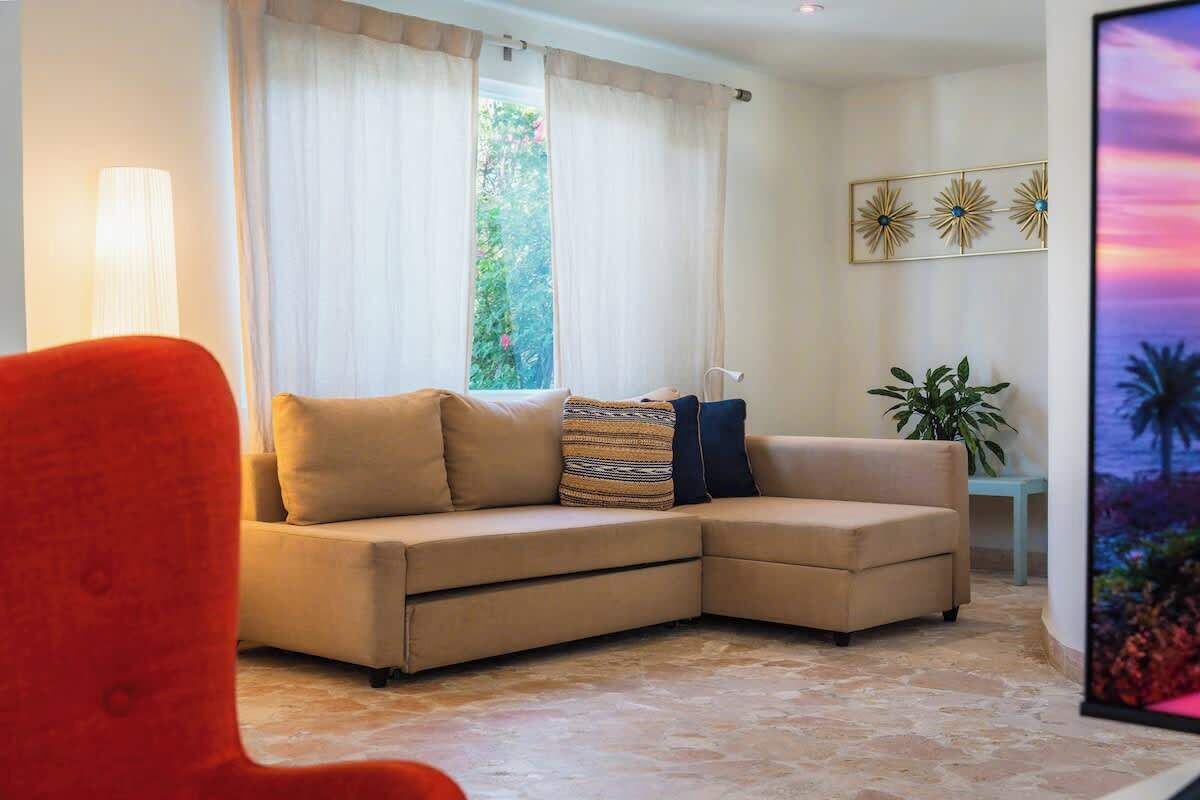 Un soggiorno con un divano modulare beige, una poltrona rossa, un tavolino con una pianta e un elemento decorativo a parete.