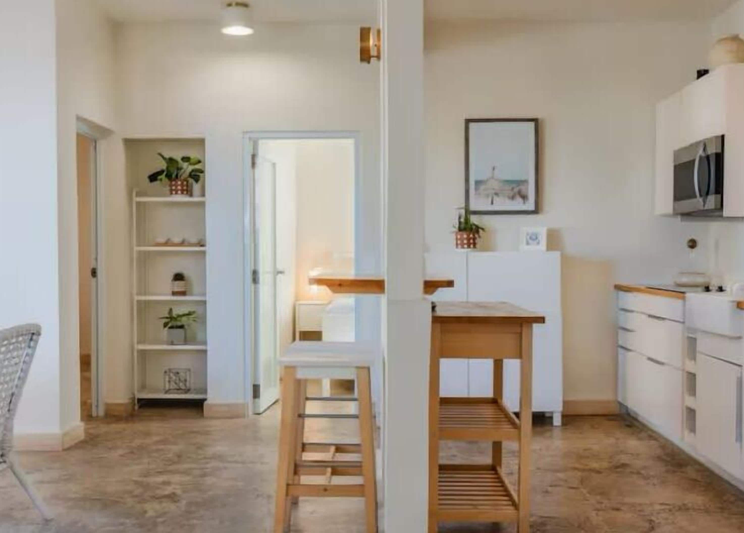 A modern kitchen with white cabinetry, a wooden table, and a built-in shelf unit.