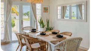 A dining area with wicker chairs, a white table, and a hanging light fixture. - Pelegrina Beach Haus 6BR Chef Powered G SJ (San Juan)