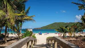 A wooden pathway leading to a beach with palm trees and umbrellas. - Villa Costera 904 Island Escapade Culebra (Culebra)