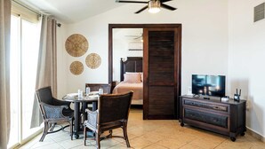 A hotel room with a dining table, chairs, a television, a ceiling fan, and a bed with a wooden headboard. - Villa Costera 904 Island Escapade Culebra (Culebra)