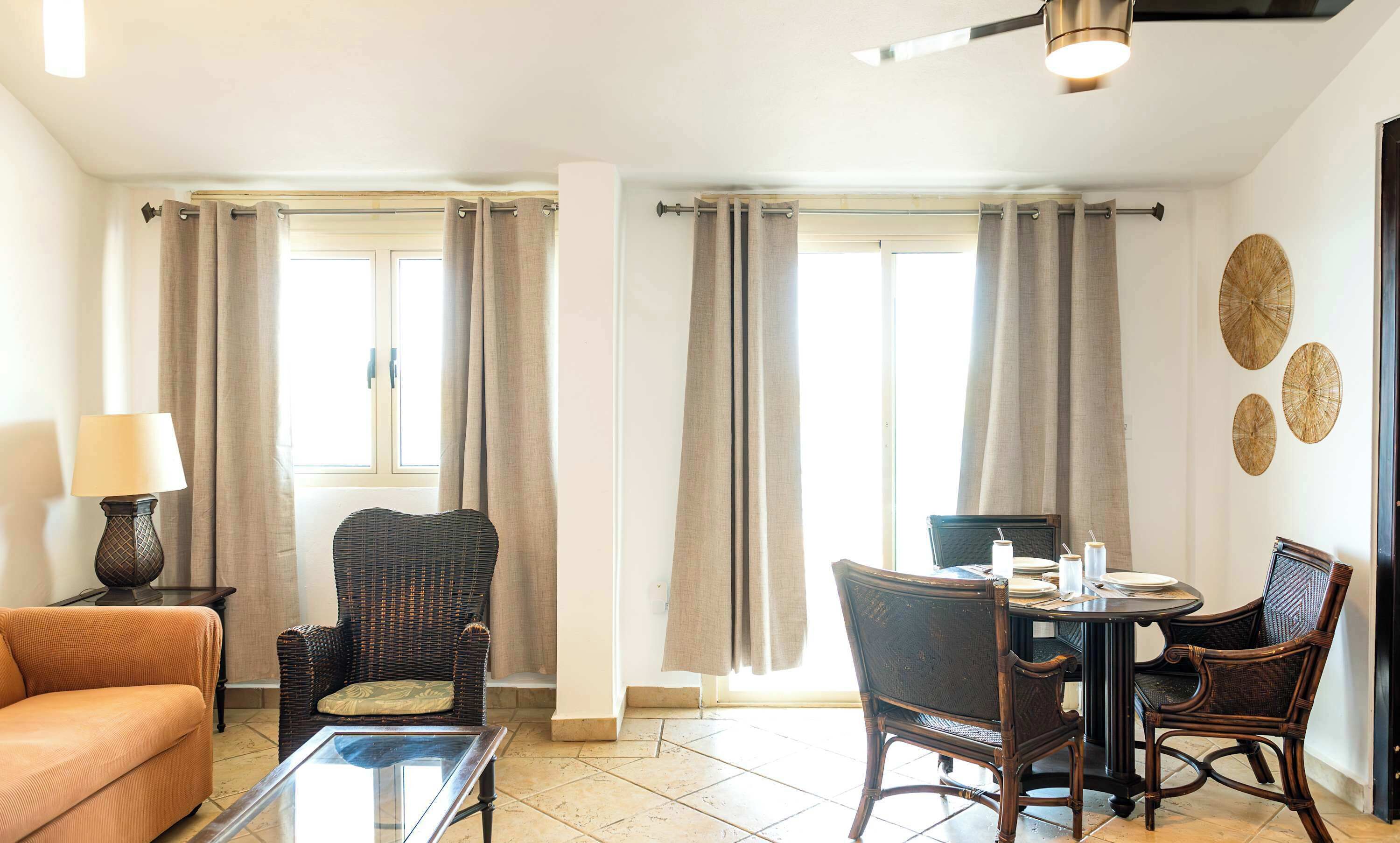 A room with a sofa, a chair, a dining table with chairs, a lamp, and a ceiling fan.