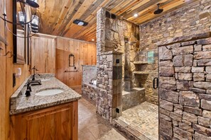 A bathroom with a stone wall, wooden ceiling, and a glass-enclosed shower. - Luxury Riverfront Retreat • Spa • Game Room • Minutes to Downtown Blue Ridge (Blue Ridge)