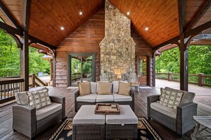 A covered outdoor seating area with wicker furniture and a stone fireplace. - Luxury Riverfront Retreat • Spa • Game Room • Minutes to Downtown Blue Ridge (Blue Ridge)