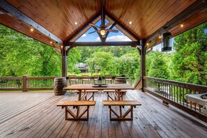 Eine Holzterrasse mit Picknicktischen und Bänken, einem Deckenventilator und Blick auf eine üppige grüne Landschaft.