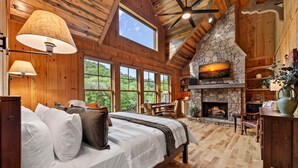 Ein Schlafzimmer mit einem großen Bett, einem Kamin aus Stein und Blick ins Freie.