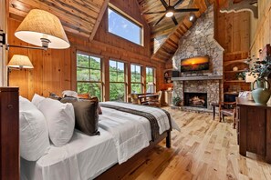 Ein Schlafzimmer mit einem großen Bett, einem Kamin aus Stein und Blick ins Freie.