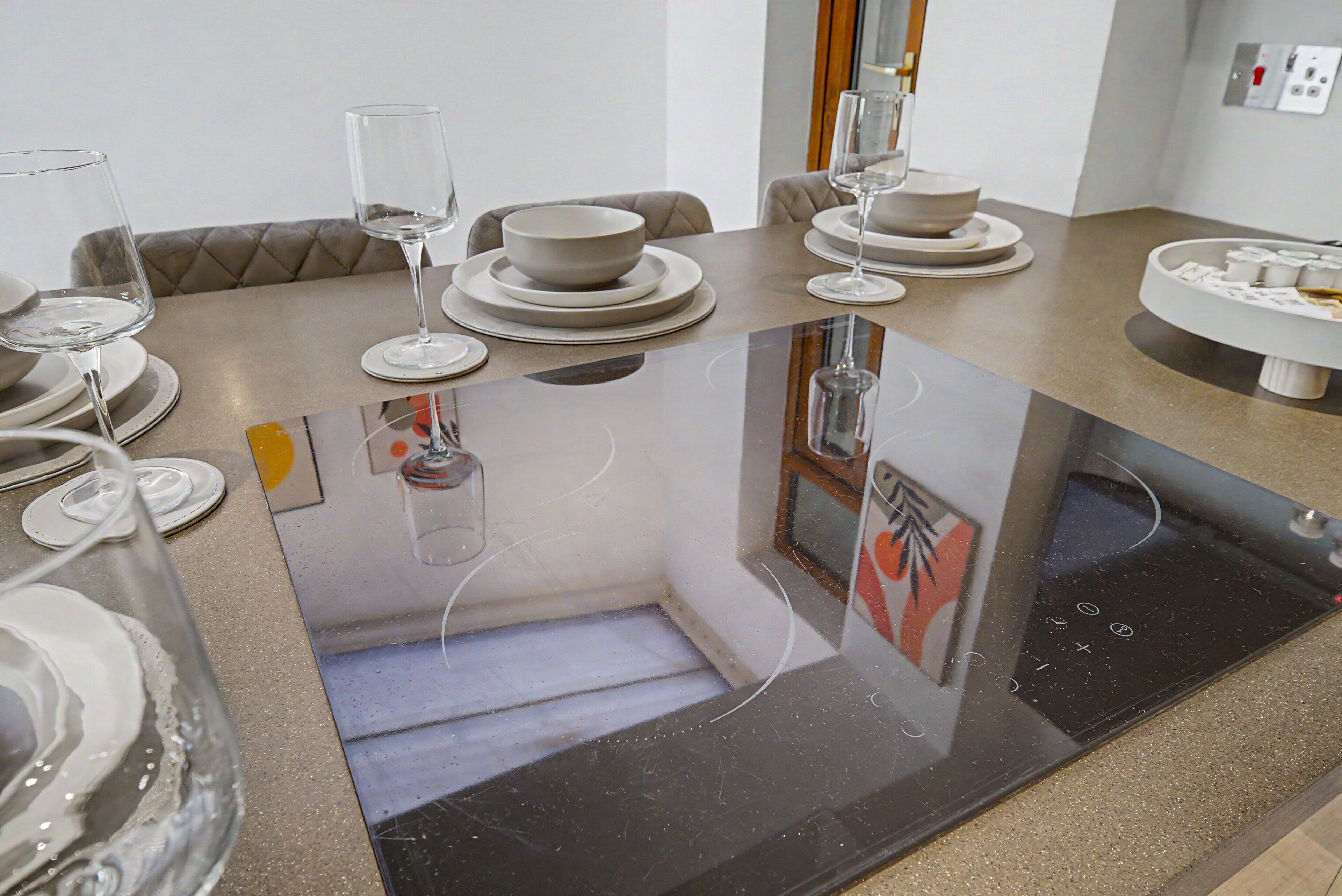 A modern dining area with a glass table, white plates, bowls, and wine glasses.