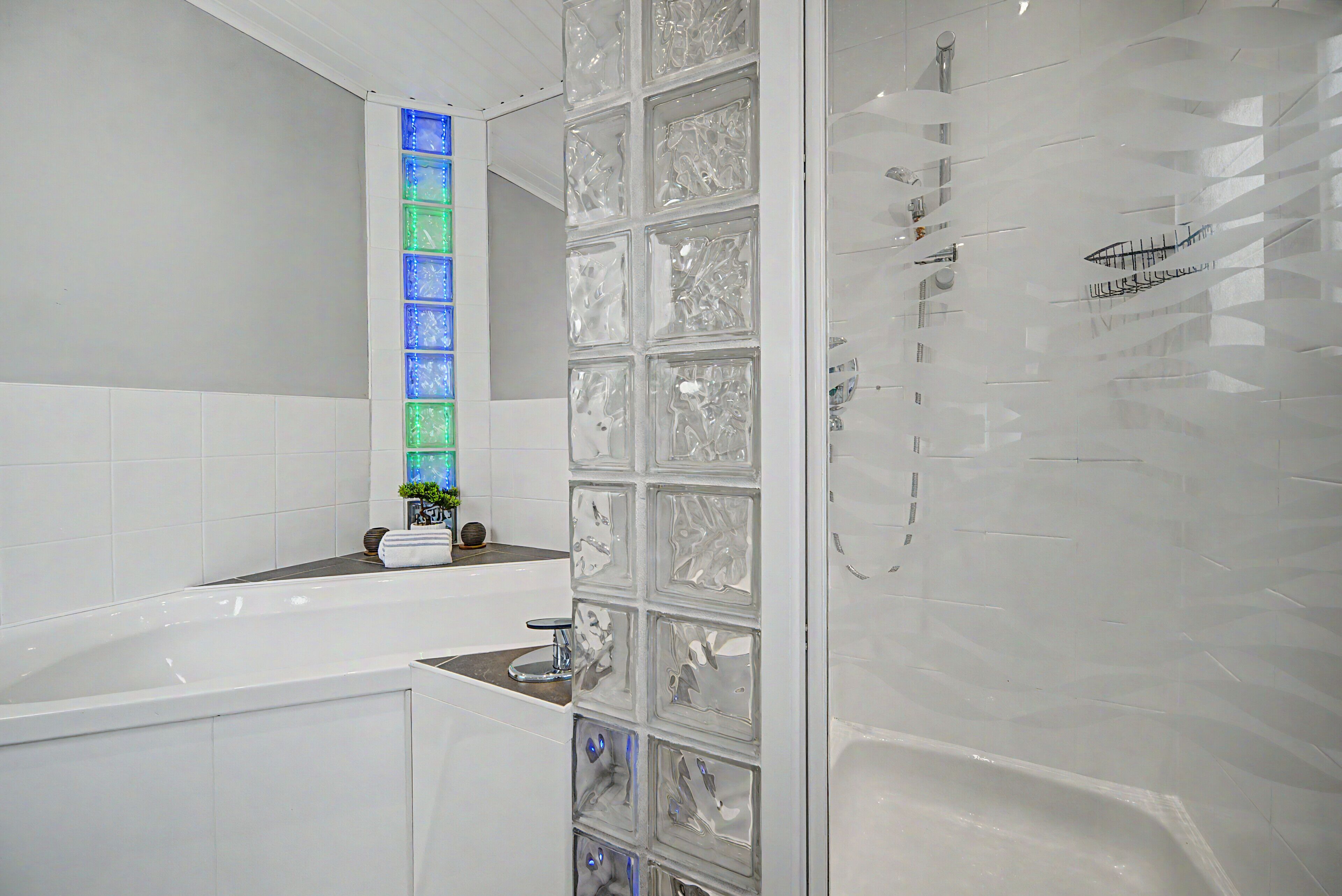 Un baño moderno con cabina de ducha de vidrio, una bañera blanca y una pared con revestimiento de azulejos y un elemento decorativo de iluminación vertical.