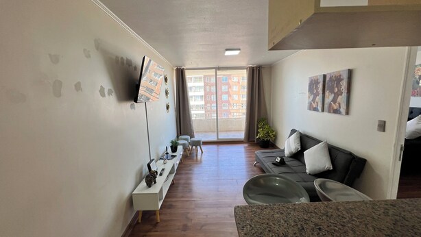 A modern living room with a sofa, a TV, a dining table, and a balcony with a view of buildings. - Cozy apartment in front of Torpederas beach, ideal for resting. (Valparaíso)
