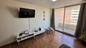 A living room with a TV, a white console table, a sofa, and a balcony with a view of buildings. - Cozy apartment in front of Torpederas beach, ideal for resting. (Valparaíso)