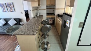 A compact kitchen with a granite countertop, stainless steel appliances, and a dining area with a sofa and bar stools. - Cozy apartment in front of Torpederas beach, ideal for resting. (Valparaíso)