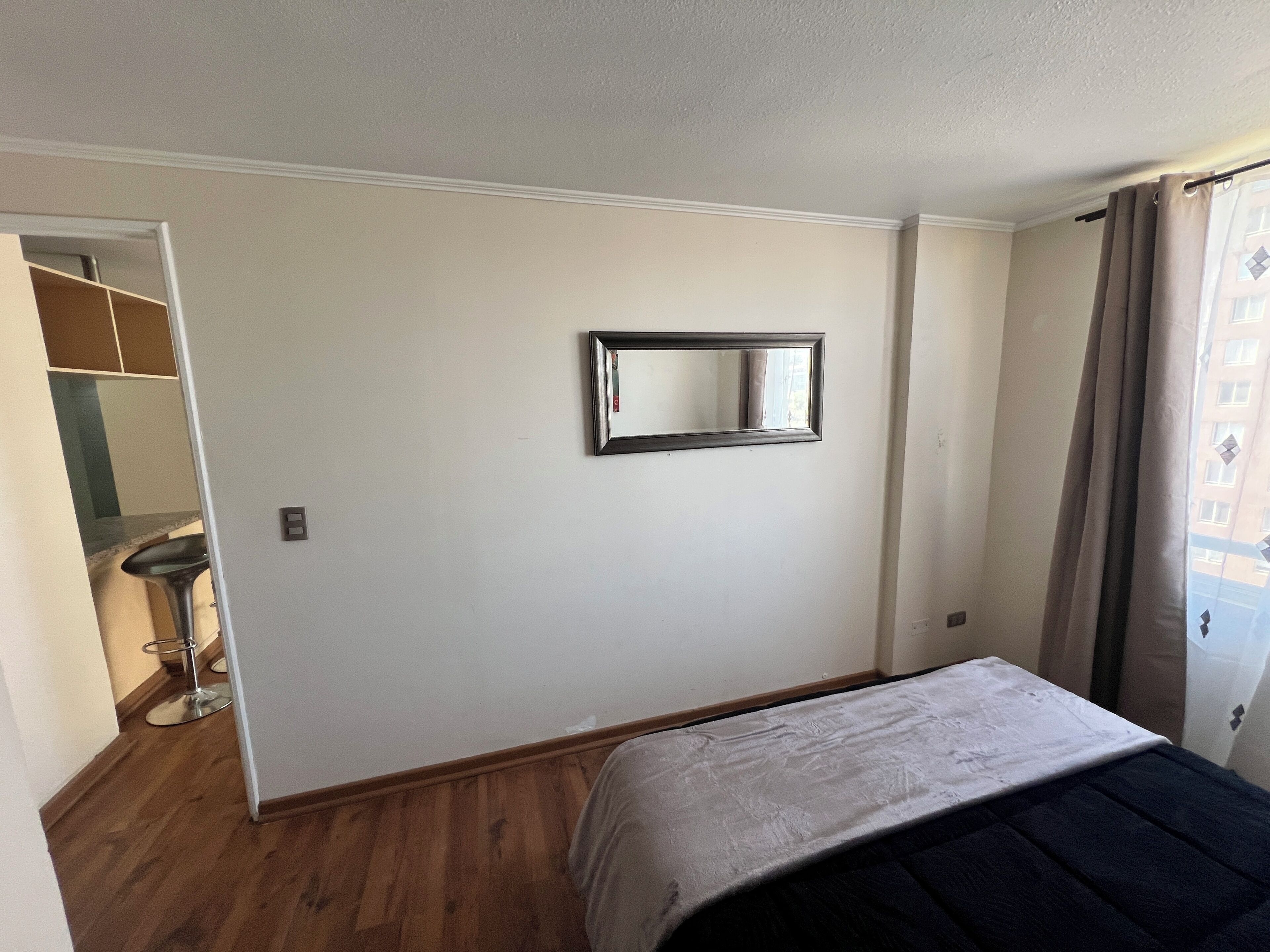Een slaapkamer met een bed, een spiegel, een kast en een raam met gordijnen.