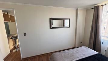 Een slaapkamer met een bed, een spiegel, een kast en een raam met gordijnen.
