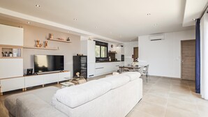 Una sala de estar moderna con un sofá grande, un televisor de pantalla plana y una zona de cocina con armarios blancos y una mesa de comedor.