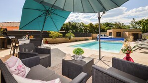 Un patio exterior con mobiliario de mimbre, una piscina y una sombrilla grande.