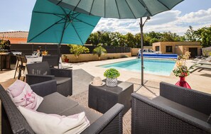 Eine Terrasse im Freien mit Korbmöbeln, einem Pool und einem großen Sonnenschirm.