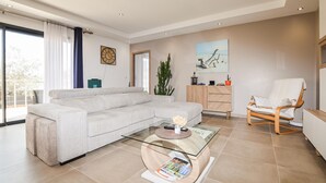 Una sala moderna con un sofá, una mesa de centro de vidrio, un armario de madera, una silla y un cuadro en la pared.