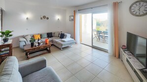 Una sala de estar con sofá, mesa de centro, televisor y puerta corrediza de vidrio que da a un espacio exterior.