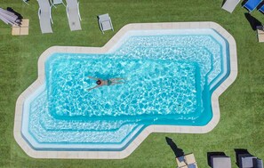 Ein rechteckiger Pool mit einer Person, die schwimmt, umgeben von einer Rasenfläche und Liegestühlen.