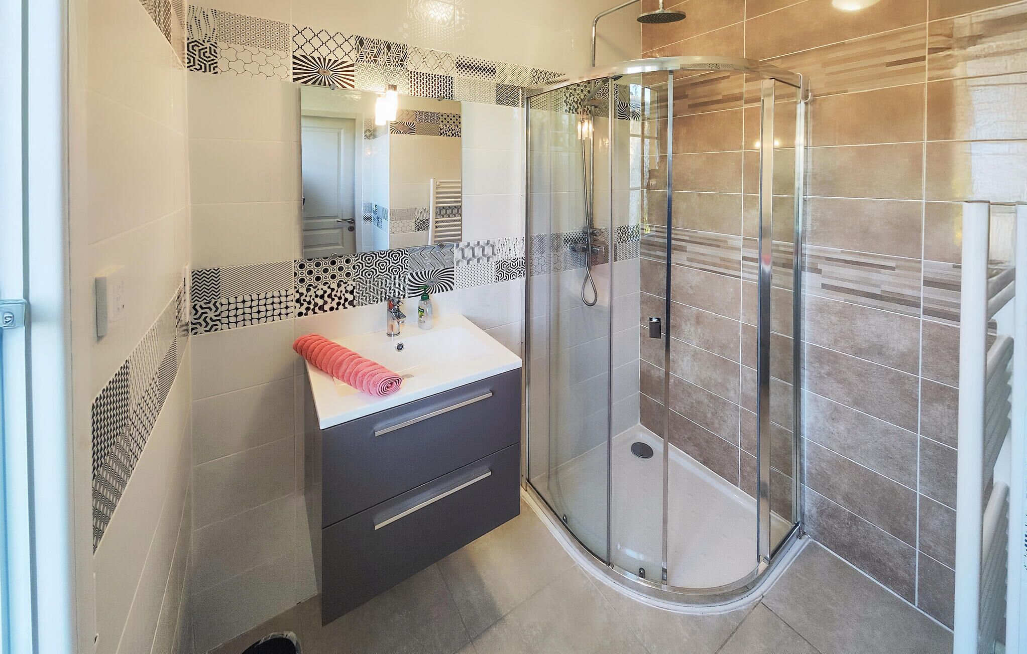 A modern bathroom with a glass-enclosed shower, a vanity with a mirror, and patterned tiles on the walls.