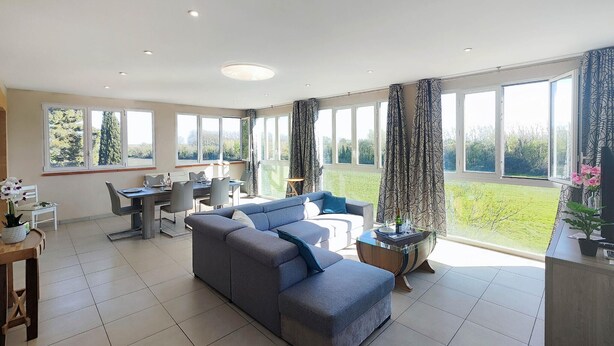 A spacious living area with a sofa, dining table, and chairs, large windows with curtains, and a view of greenery outside. - Gorgeous apartment in Mirepeisset with WiFi (Mirepeisset)