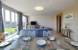 Un salon moderne avec un canapé, une table à manger pour six personnes et un téléviseur.