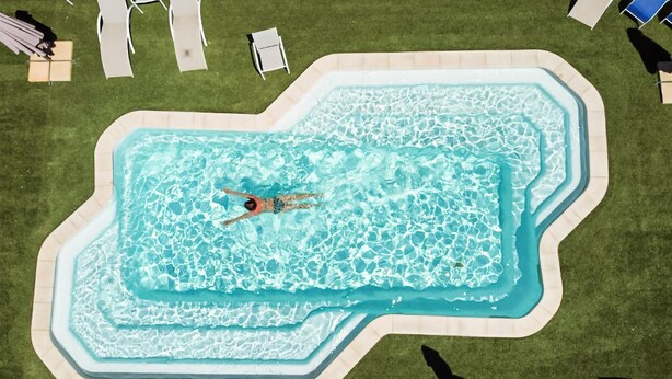 An aerial view of a swimming pool with a person swimming, surrounded by lawn chairs and umbrellas. - Gorgeous home in Mirepeisset with outdoor swimming pool (Mirepeisset)