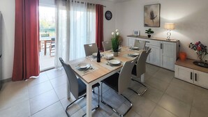 Un comedor con una mesa dispuesta para cuatro, un reloj en la pared y una planta en la encimera.