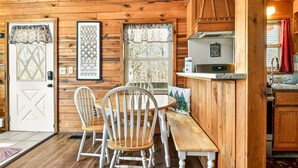 Een houten chalet van binnen, met een eethoek, keuken en kunstwerken in lijsten aan de muren.