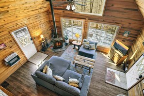 A cabin interior with a sofa, a fireplace, a television, and a large window. - Serenity Woods - Fireside Relaxation, Pet-Friendly Fun & Scenic Gazebo Views (Blue Ridge)