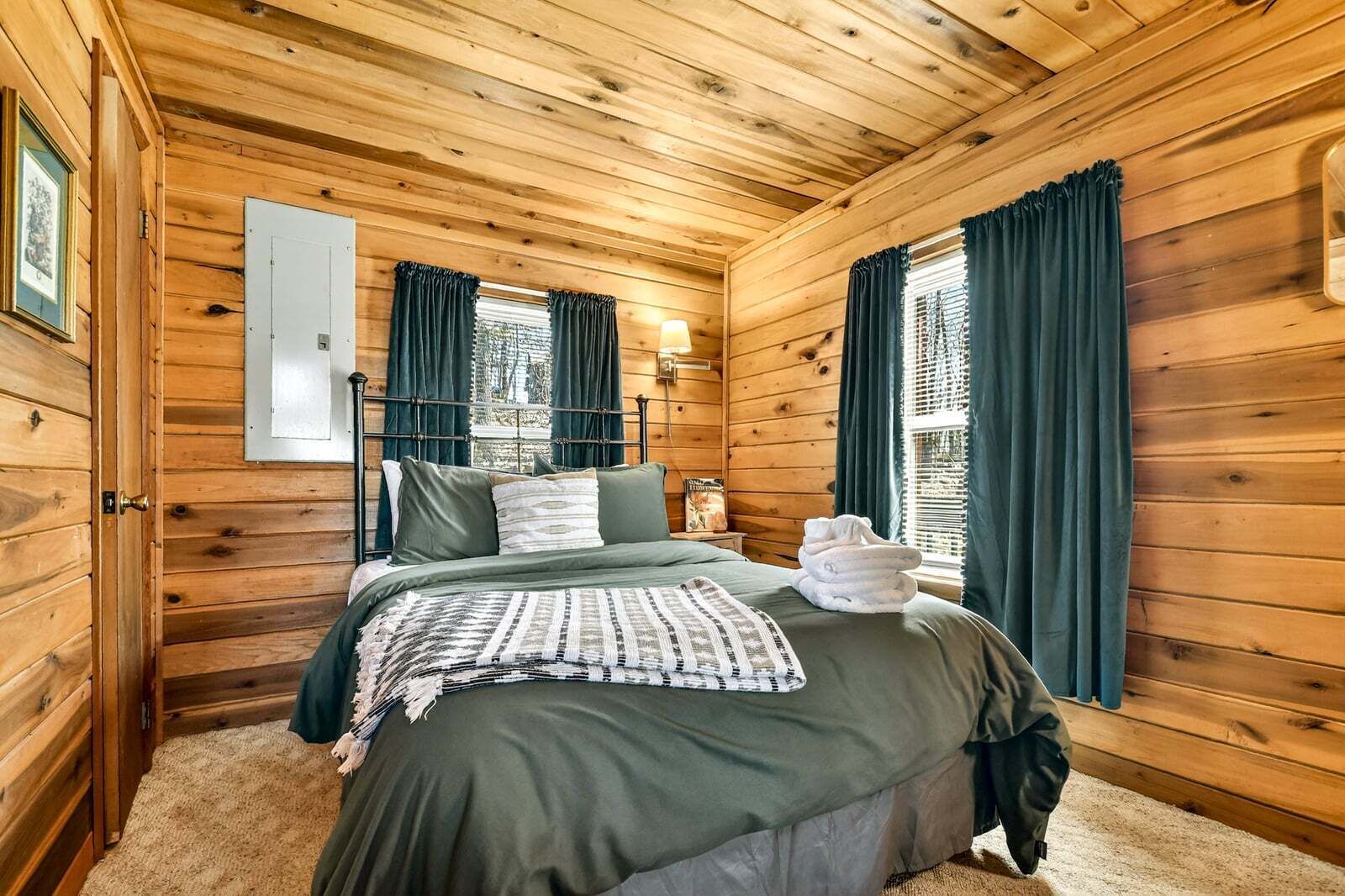 A wooden cabin bedroom with a bed, curtains, and a window.