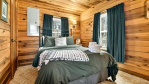 Een houten slaapkamer met een bed, gordijnen en een raam.