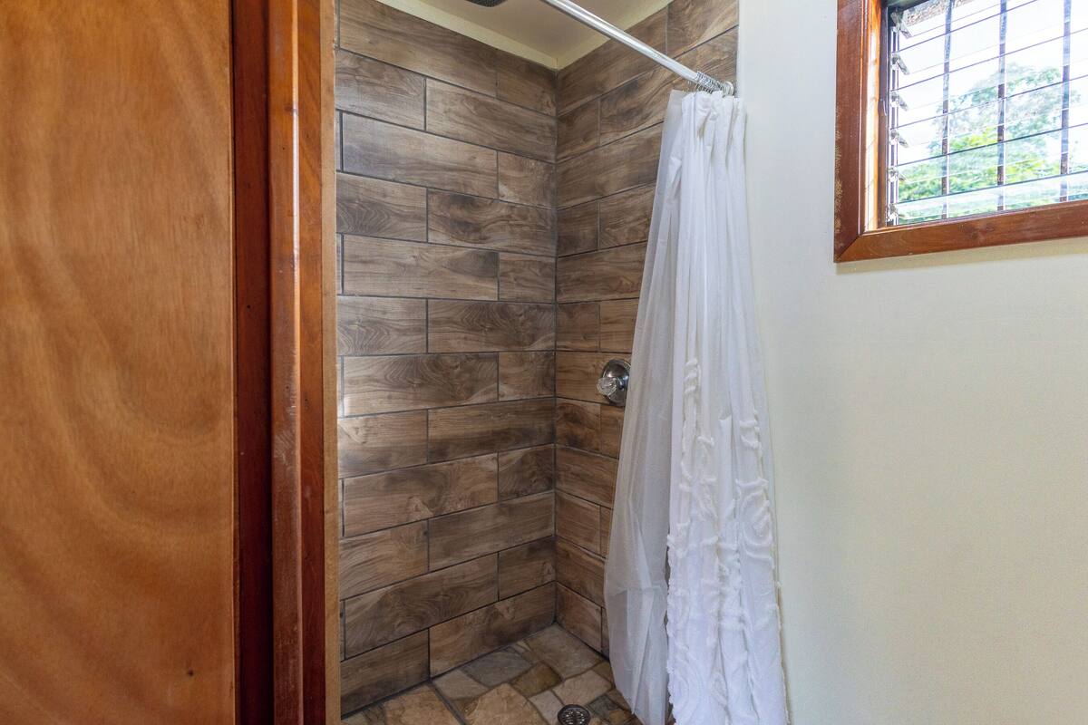 A shower with wooden tiles, a white curtain, and a window with a grid pattern.
