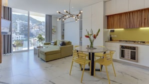 Ein modernes Apartment mit Essbereich, Sofa, Küche und großen Fenstern mit Blick auf die Stadt.