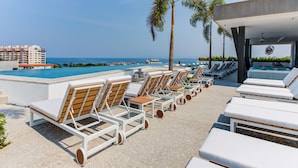 Ein Poolbereich mit Liegestühlen, Palmen und Blick aufs Meer.