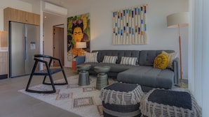 A modern living room with a sofa, a chair, a table, and a painting on the wall. - Oasis 408: Oasis Riverfront Luxury 2BR Infinity Pool & Views (Puerto Vallarta)