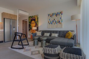 A modern living room with a sofa, a chair, a table, and a painting on the wall. - Oasis 408: Oasis Riverfront Luxury 2BR Infinity Pool & Views (Puerto Vallarta)