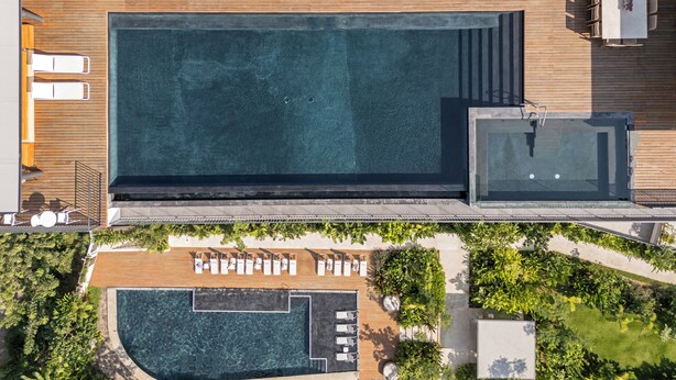 An aerial view of a resort with a large rectangular swimming pool, multiple lounge areas with sunbeds, and a separate hot tub area. - Oasis 408: Oasis Riverfront Luxury 2BR Infinity Pool & Views (Puerto Vallarta)
