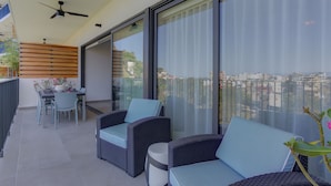 A balcony with wicker furniture, a table with chairs, and a view of the cityscape. - Oasis 408: Oasis Riverfront Luxury 2BR Infinity Pool & Views (Puerto Vallarta)