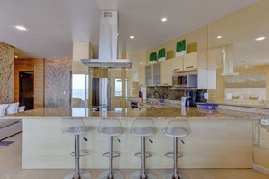 A modern kitchen with a central island, bar stools, stainless steel appliances, and a large window. - Gorgeous Ocean Views+Private Plunge Pool+Balcony (Puerto Vallarta)