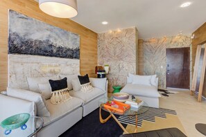 A modern living room with two sofas, a coffee table, a large abstract painting, and a wooden accent wall. - Gorgeous Ocean Views+Private Plunge Pool+Balcony (Puerto Vallarta)