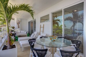 A modern indoor space with a glass table surrounded by wicker chairs, white sofas, and potted plants. - Gorgeous Ocean Views+Private Plunge Pool+Balcony (Puerto Vallarta)