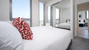 Ein modernes Hotelzimmer mit einem großen Bett, Blick auf die Stadt und einer Schiebetür zu einem weiteren Raum.