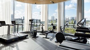Ein modernes Fitnessstudio mit Laufbändern, Crosstrainern und Krafttrainingsgeräten, große Fenster mit Blick auf die Stadt.