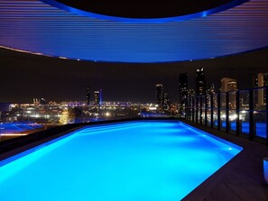 Piscina infinita en la azotea con vistas a la ciudad de noche.