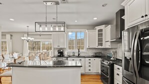 Una cocina moderna con armarios blancos, una isla central, electrodomésticos de acero inoxidable y un comedor con sillas.