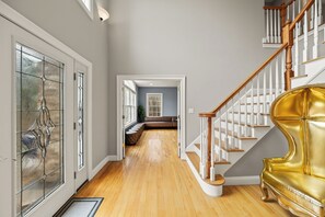 A spacious hallway with a wooden floor, a golden chair, and a staircase with white railings.