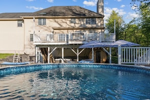 Un espace piscine résidentiel comprenant une maison, une terrasse couverte et une piscine à l’eau d’un bleu limpide.