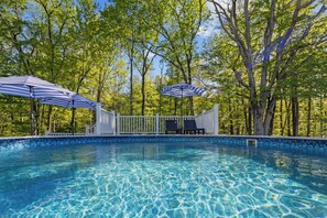 A swimming pool with clear blue water, surrounded by trees and white fencing.